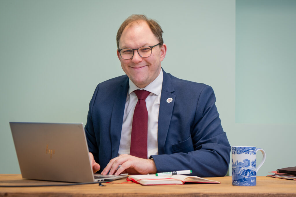 Gareth Snell sat at his desk with his laptop smiling at the camera.